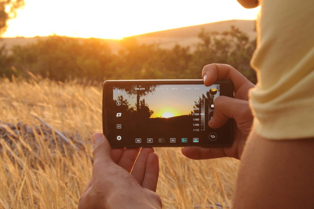 Das Bild zeigt einen Fotografen, der mit einem Smartphone einen Sonnenuntergang fotografiert.